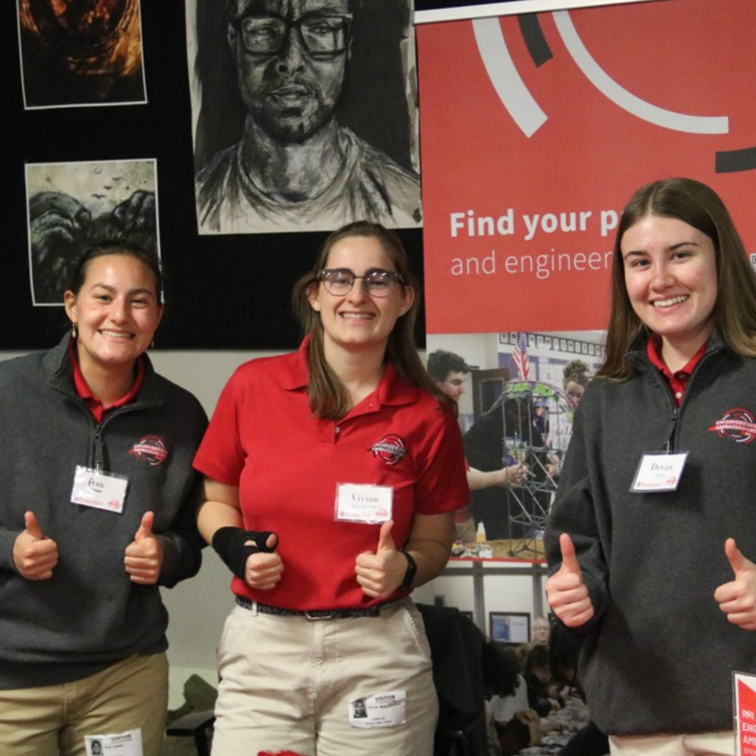 Three individuals wearing Rensselaer Engineering Ambassador name tags give thumbs up in front of a red RPI banner at an event.