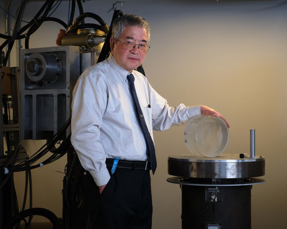 Ge Wang standing in his lab touching lab equipment and looking at the camera