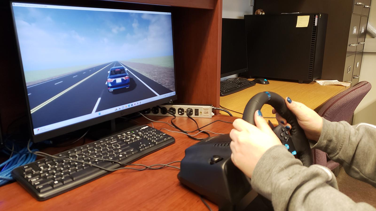 Computer screen showing car next to hands holding a steering wheel