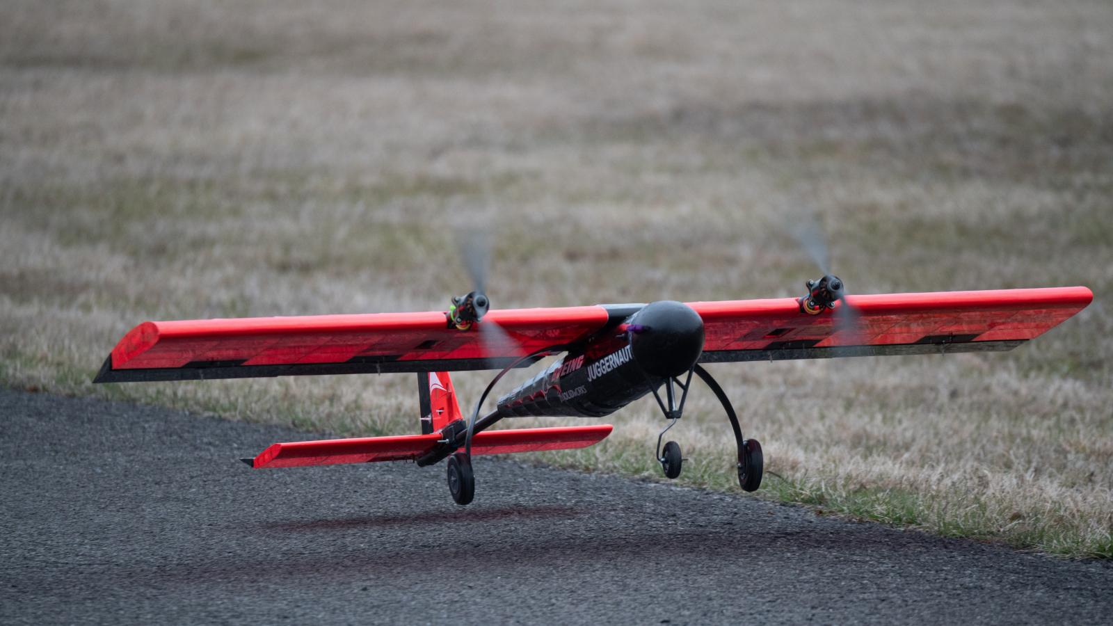 Student built aircraft taking off from the ground. Aircraft is red and black with the name Juggernaut printed on the side.
