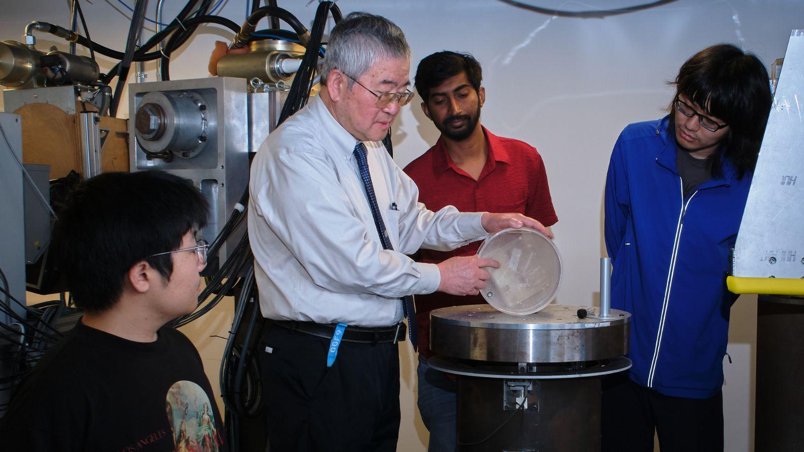 Ge Wang working with lab equipment while 3 of his students watch