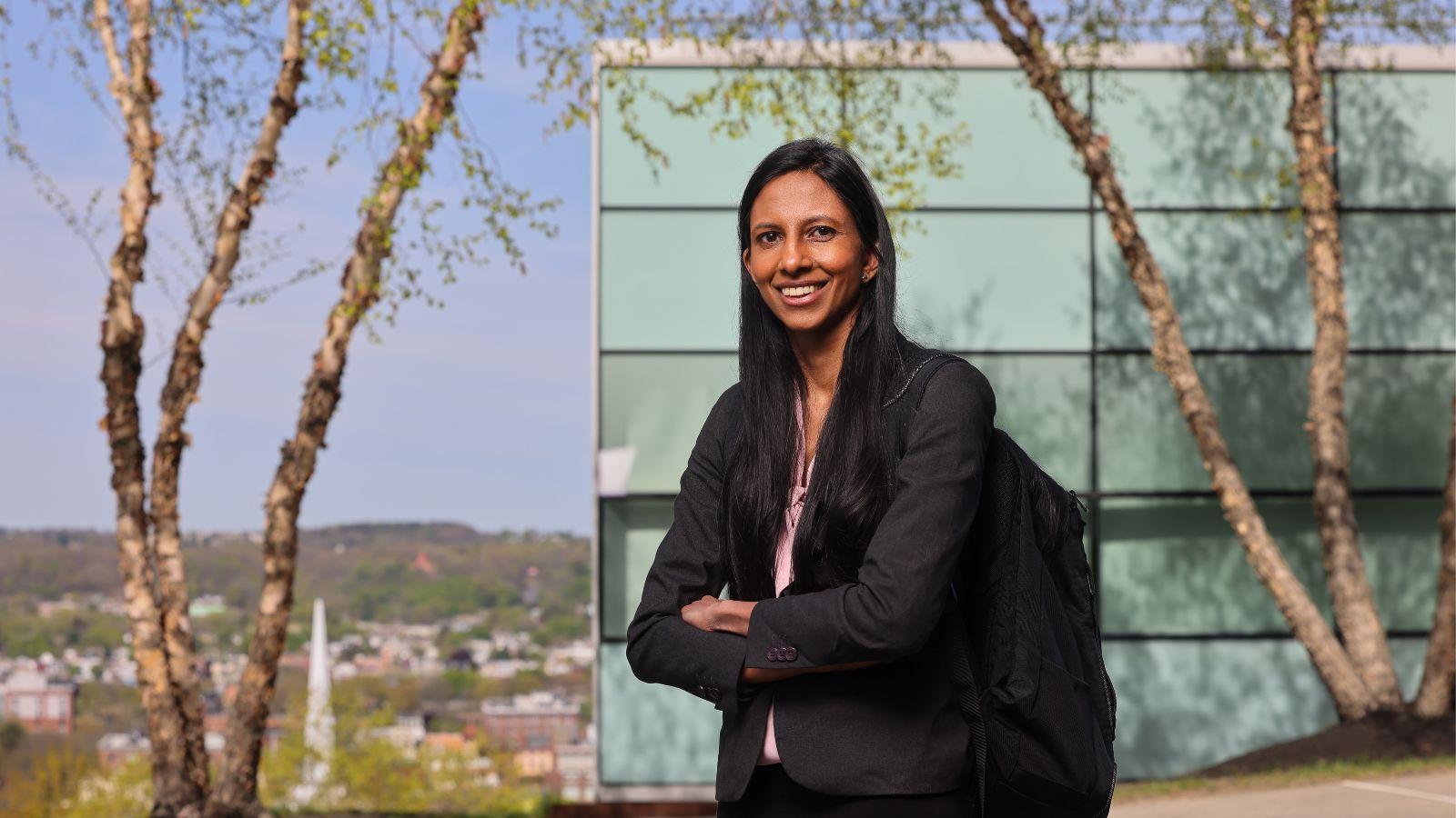 Anisha Gurumurthy standing outside smiling, posing with a backpack on one shoulder. EMPAC in the background