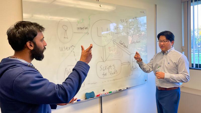 Two people have a conversation about a diagram on a white board