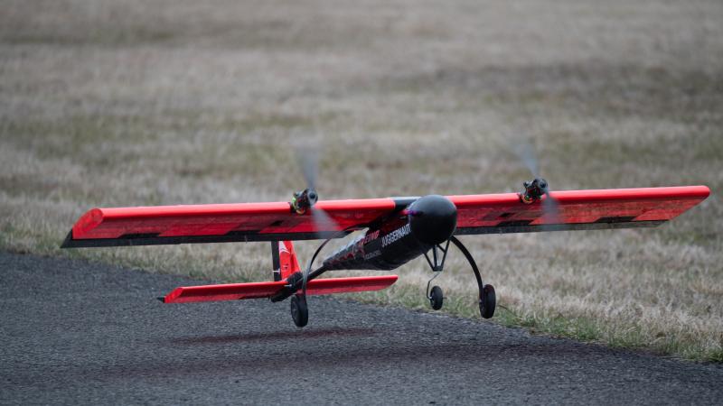 Student built aircraft taking off from the ground. Aircraft is red and black with the name Juggernaut printed on the side.
