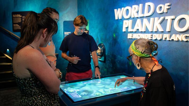 Three people interact with a digital interactive display table at the "World of Plankton" exhibit.