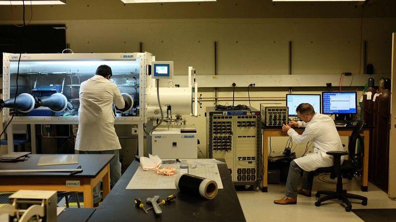 Two individuals work in a laboratory with electronic equipment and computers