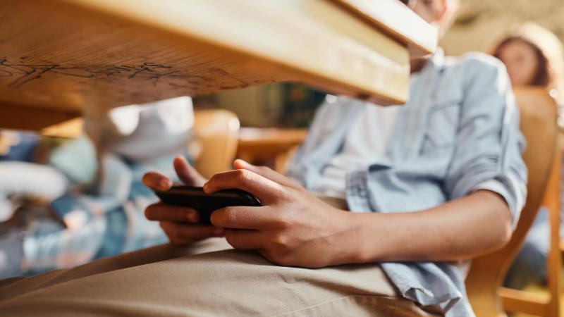 Person sitting at a desk using a smartphone under the desk