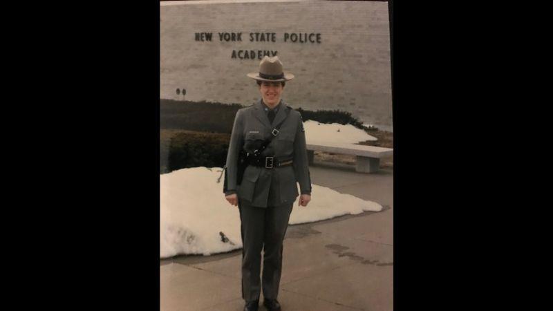 Patricia Groeber stands in uniform outside of the New York State Police Academy, smiling.