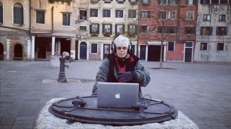 Pauline Oliveros standing outside in Venice with headphones and sunglasses on, in front of a laptop