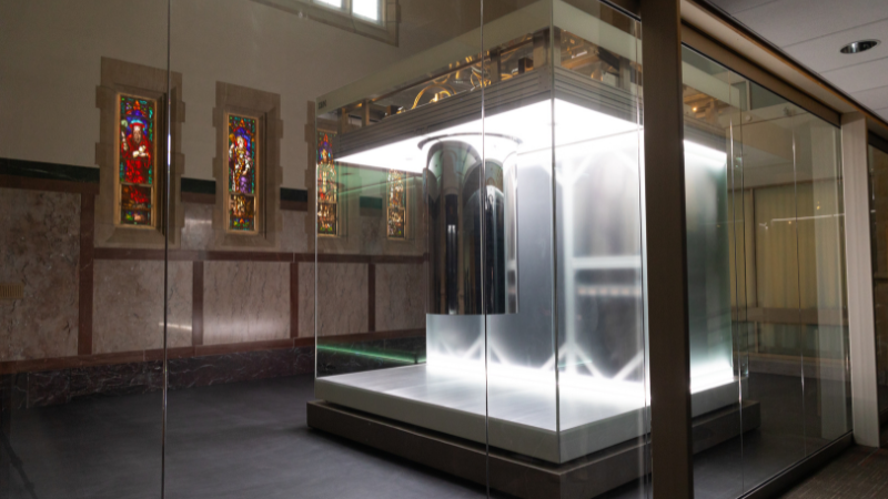 A glowing quantum computer enclosed in a glass chamber sits inside a restored chapel space. Stained-glass windows line the marble walls behind the illuminated system, highlighting the contrast between historic architecture and advanced computing technology.