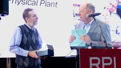 President Schmidt and Kevin Surman on stage looking at each other, Surman holding the Pillar Award