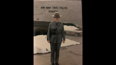 Patricia Groeber stands in uniform outside of the New York State Police Academy, smiling.